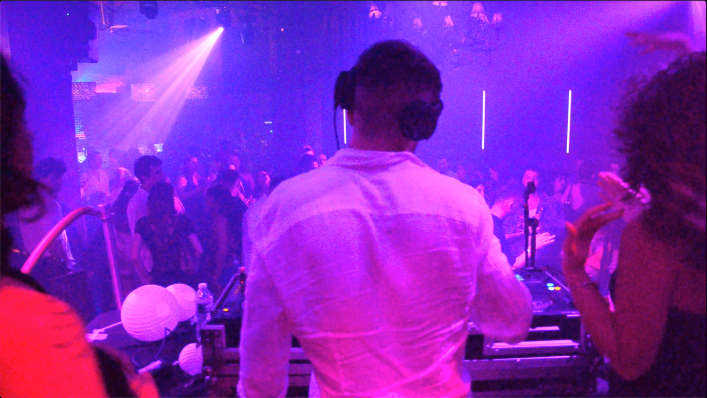 AED in a white shirt facing the crowd under purple lights at Drom