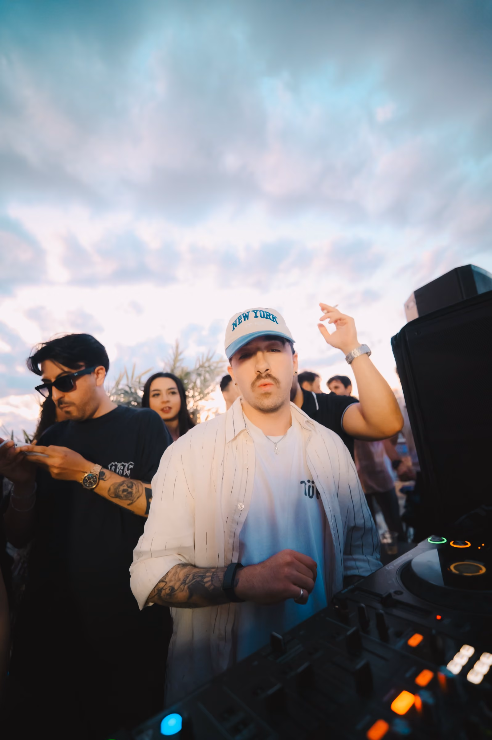 AED in a white cap playing a sunset rooftop set with the crowd behind him